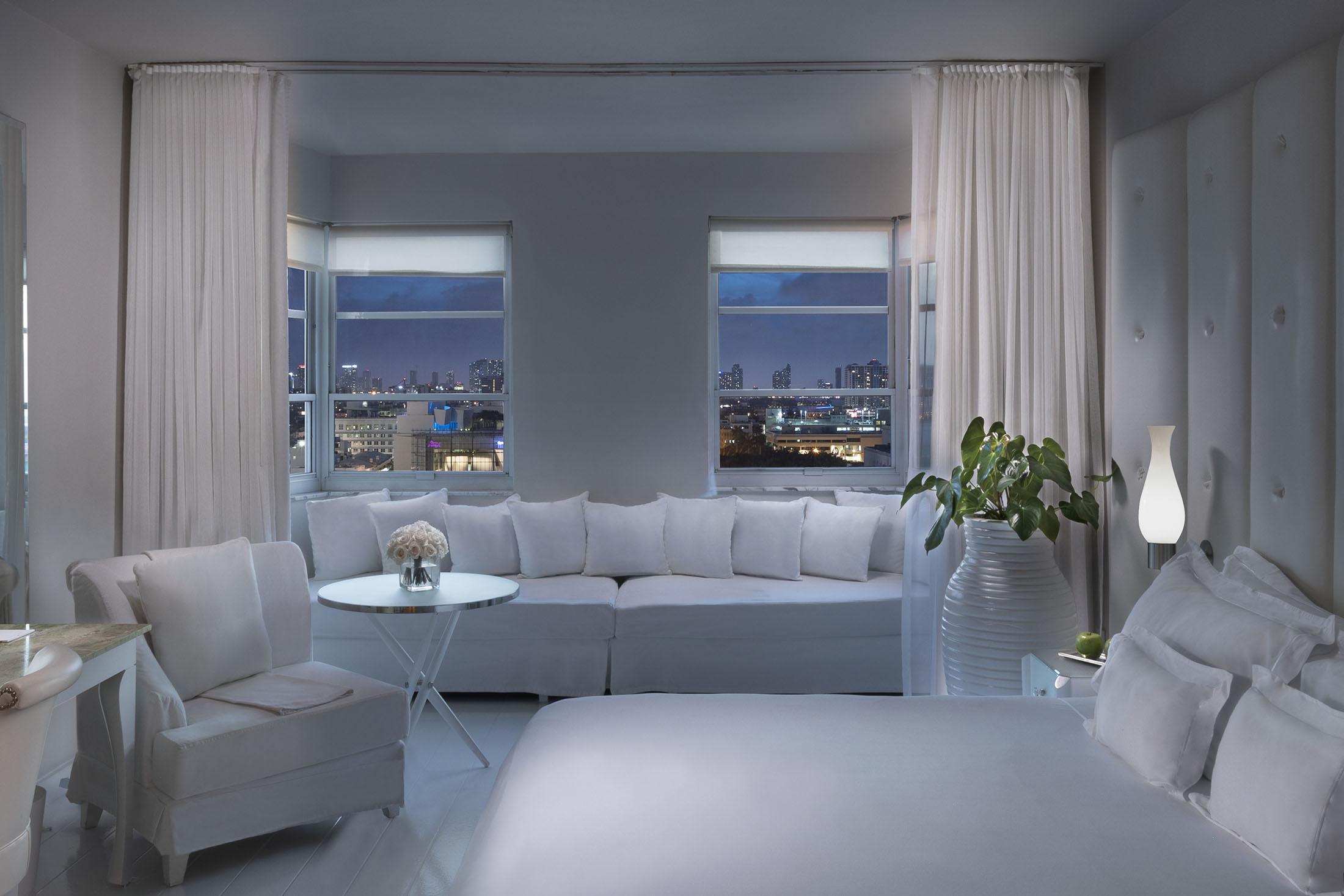 cama blanca y alcoba blanca frente a la ventana con vista a la ciudad