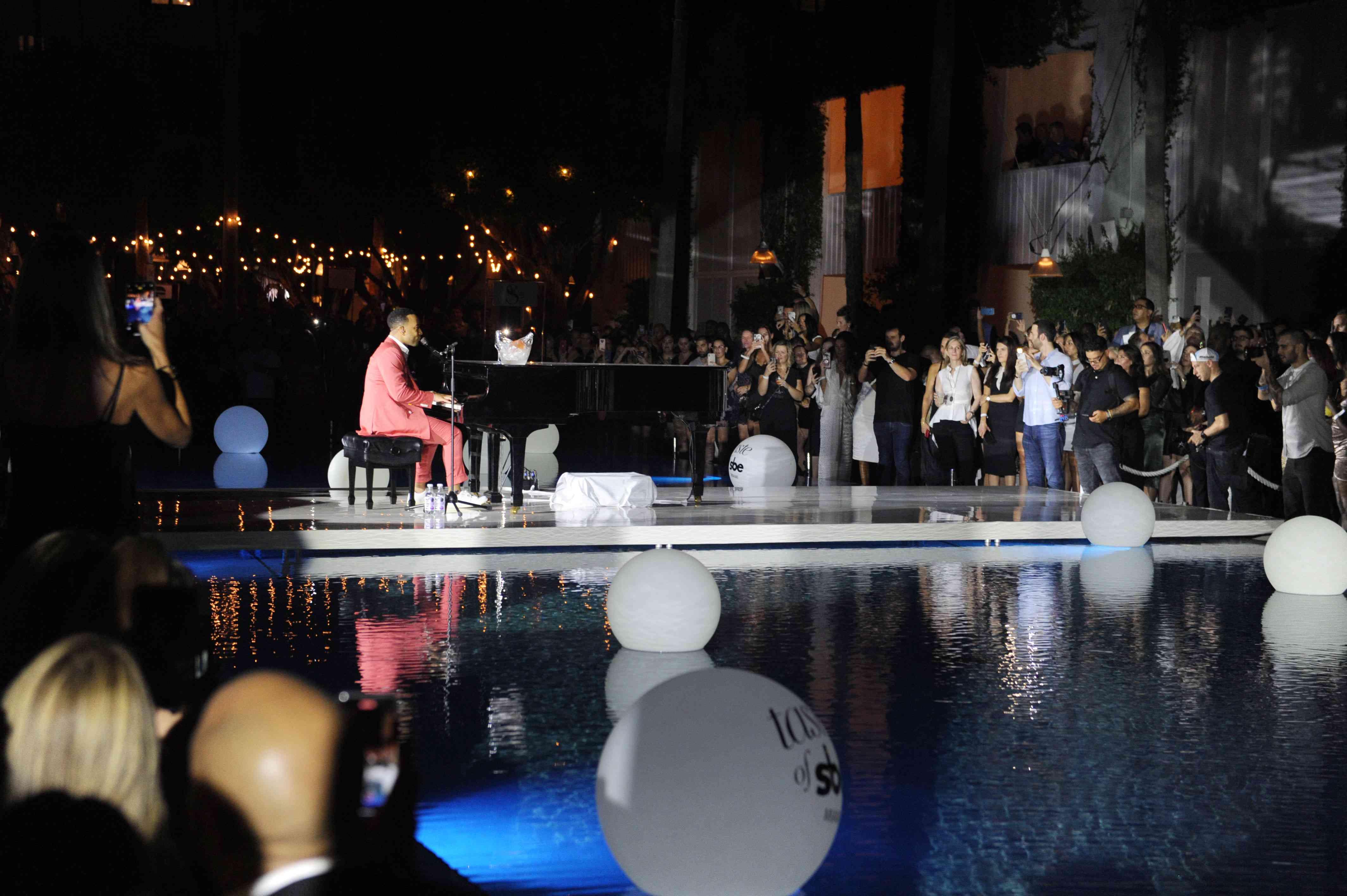 John Legend en un piano junto a una piscina
