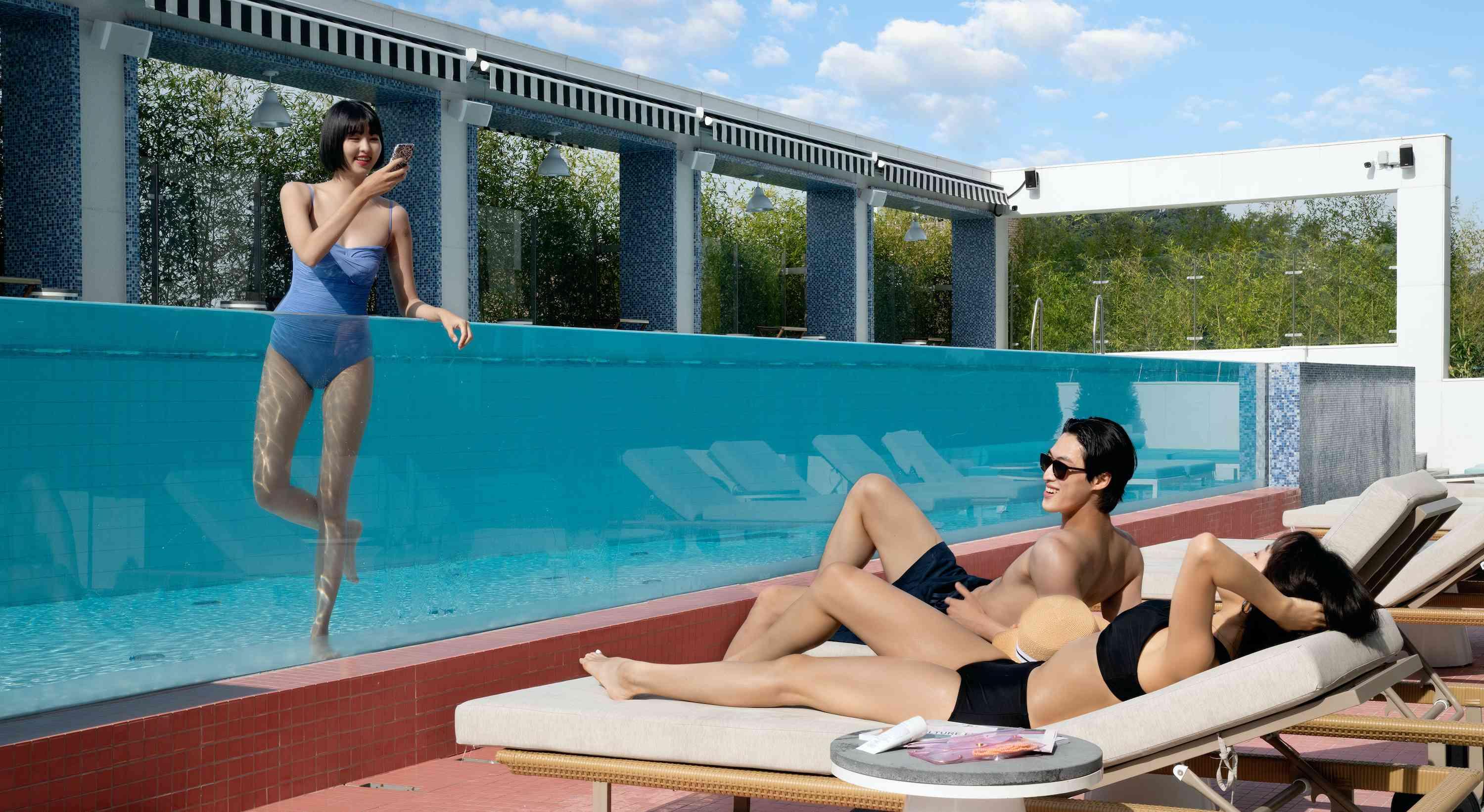 pareja en tumbonas junto a una piscina con un amigo en la piscina