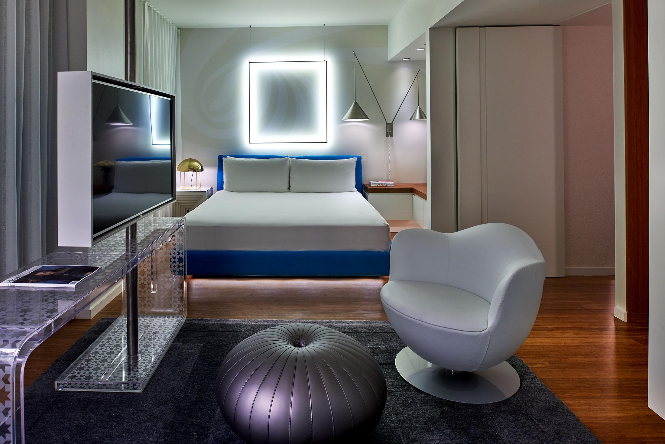Una habitación de hotel con una luz cuadrada detrás de la cama y una silla en primer plano.